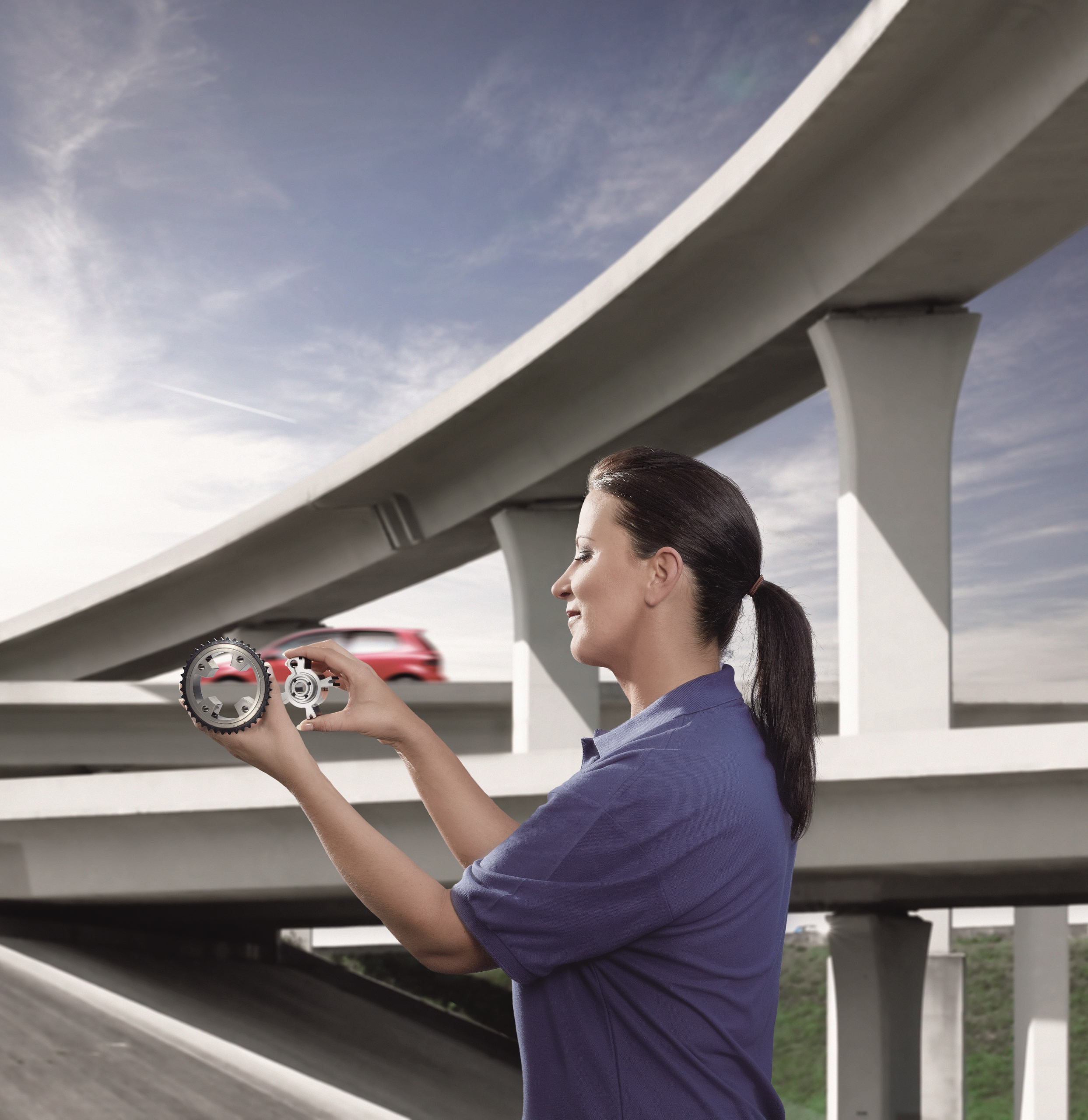 Woman holding automobile parts in front of highway overpass with passing car